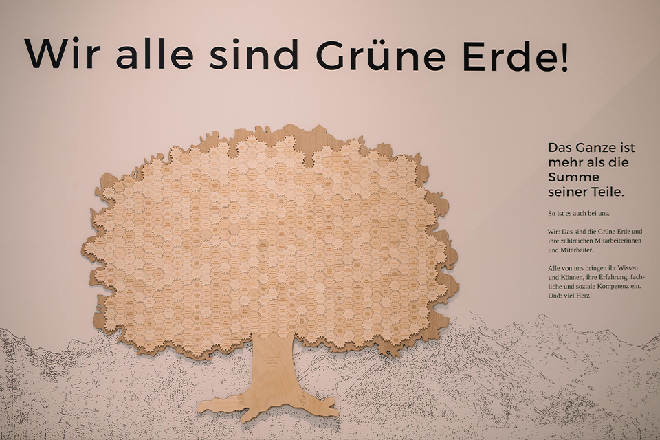 Wir alle sind Grüne Erde Schriftzug über Holzbaum mit vielen Namen auf hellem Hintergrund