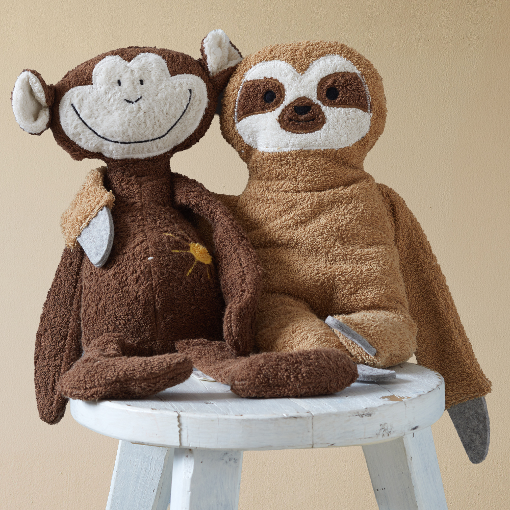 Kuscheltier-Affe und Kuscheltier-Faultier sitzen auf einem Hocker